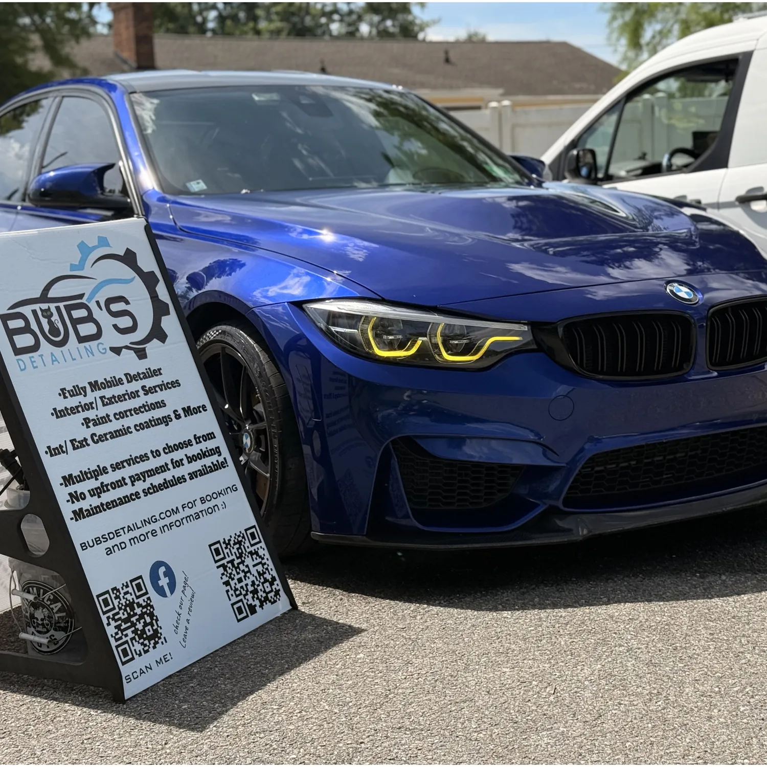 The Bub's Detailing van and sign parked beside a blue BMW M3 at a customer's home